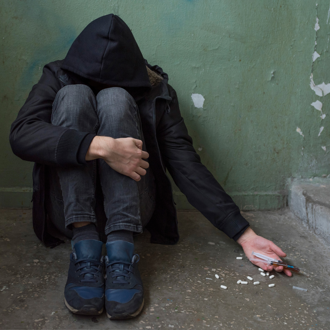 A man wearing a hoodie letting go of the drugs in his hand