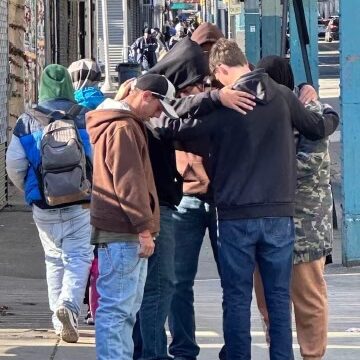 Group of men praying on a busy city sidewalk