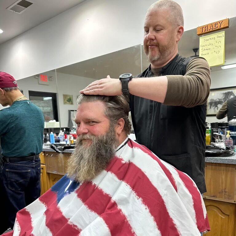 Bearded man wearing a US flag barber's covering as he gets a haircut