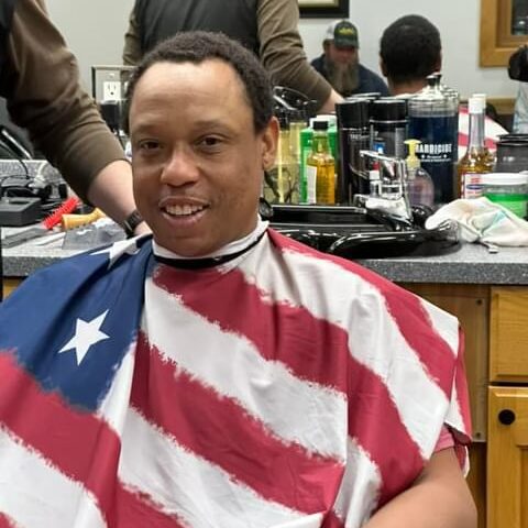 Young man wearing a US flag barbers apron as he gets his haircut