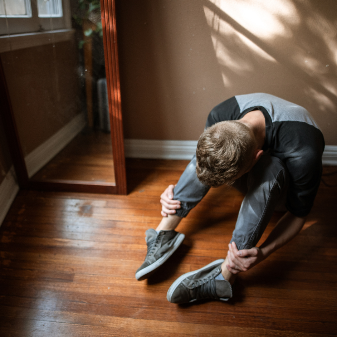 Man curled up on a wooden floor in emotional anguish with a mirror beside him